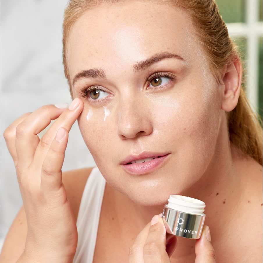 A woman patting the night eye cream under her eye, the open jar in her other hand.