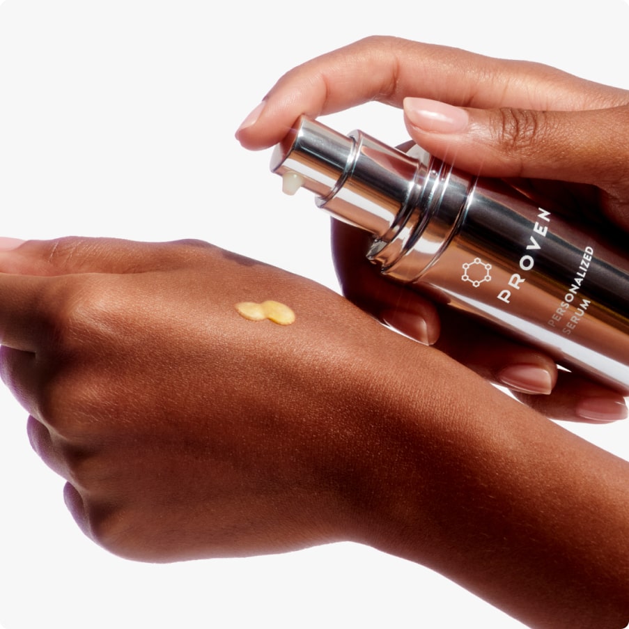 A hand pressing the serum pump over the back of the other hand, a golden drop on the skin.
