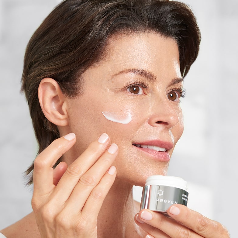 A woman applying a stripe of Personalized Night Cream to her cheek, the open jar in her hand.