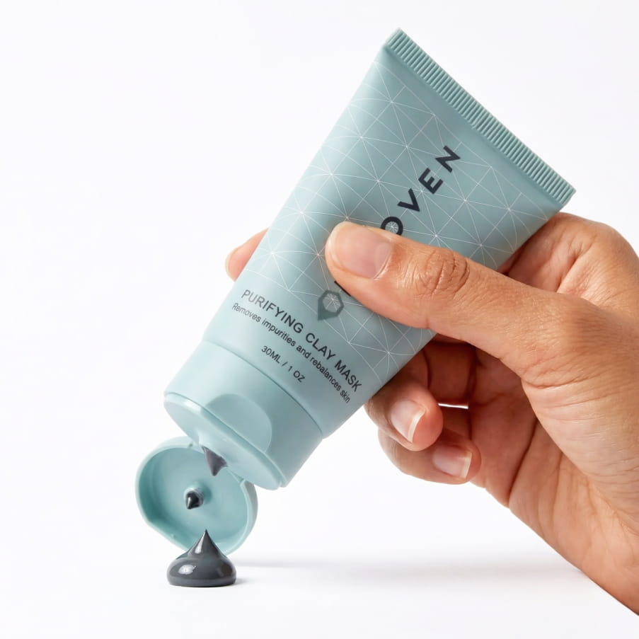 A hand squeezing the tube, with the dark grey clay mask coming out of the nozzle