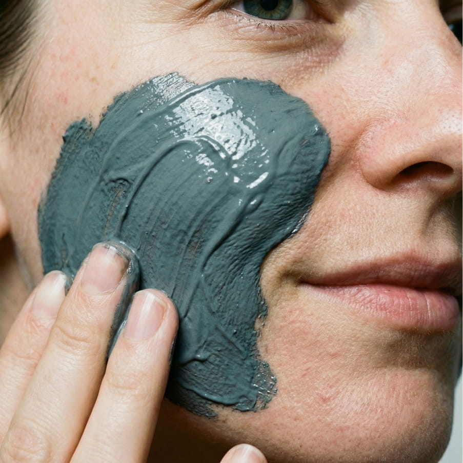 The grey clay mask being spread across a cheek with two fingers