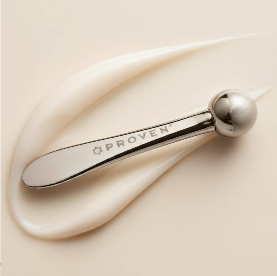 The applicator resting on a swipe of cream, showing its flat paddle end and polished ball tip.