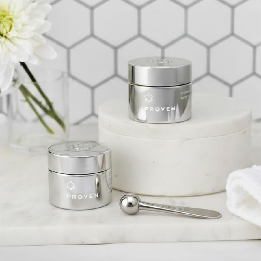 The applicator on a marble counter beside two silver PROVEN eye cream jars.